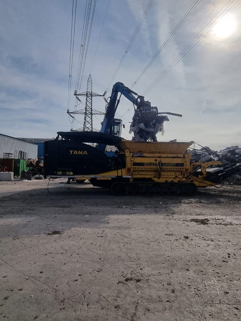 Material handler with grab sorting waste above the shredder hopper